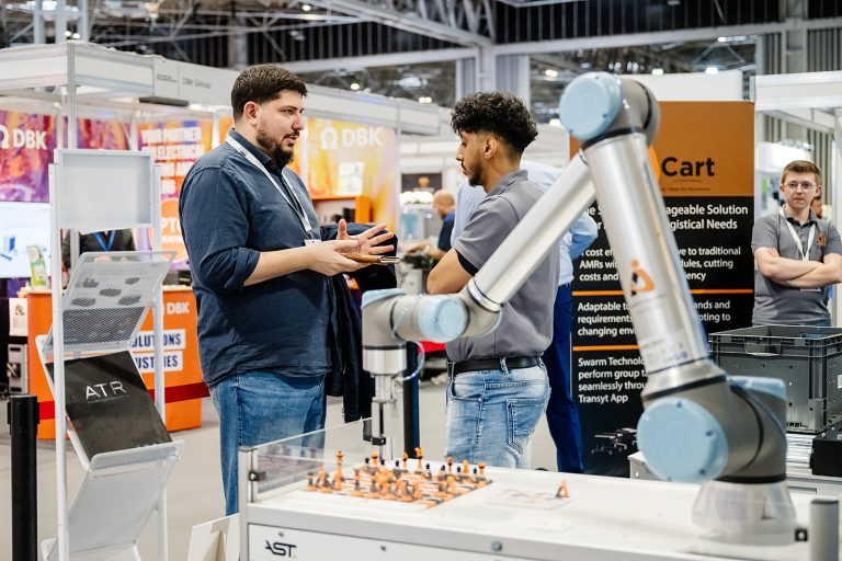 Advanced Engineering 2026 Innovation Gallery preview: visitors talk beside a collaborative robot arm demo on an exhibitor stand